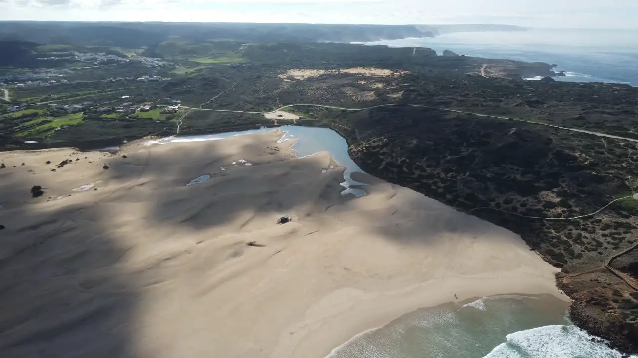 drone pans over amazing bordeira beach in the algarve in portugal waves in the bay with sunny weather