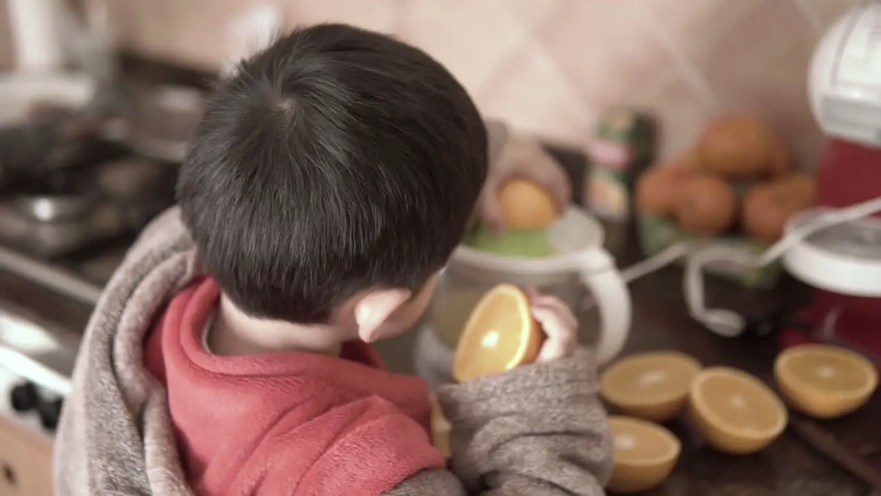 Asian kid holding oranges and making juice with an electric squeezer