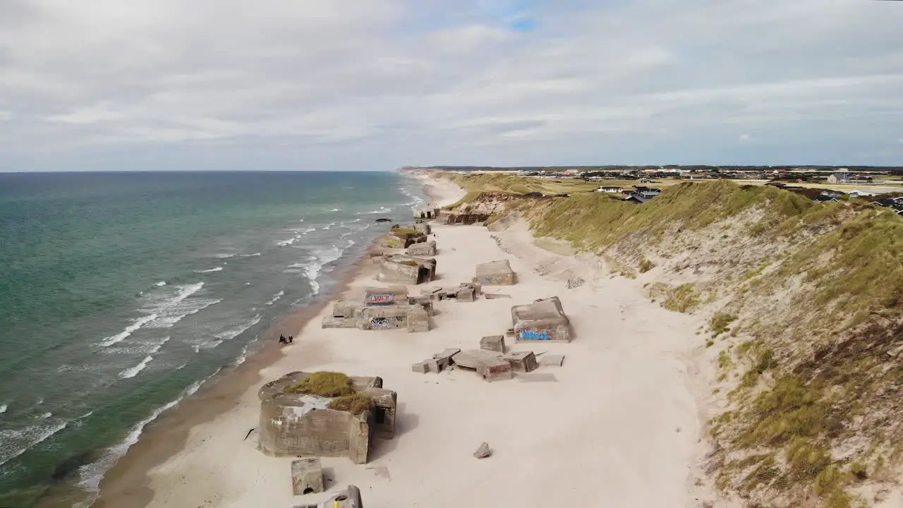 Aerial dolly out of the long white sanded beach on the Danish coastline with several old abandoned German bunkers in the sand on a cloudy summer day