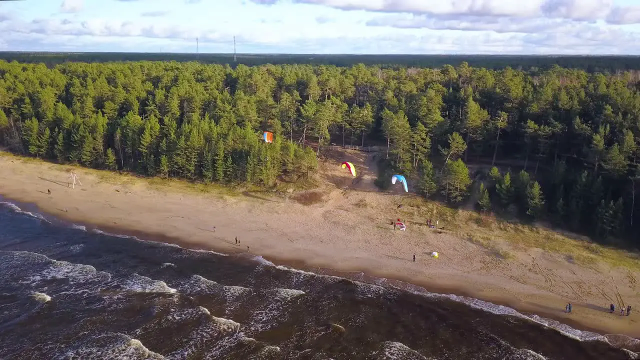 Tourists enjoying parasailing on sandy beach with calm waves reaching the shore