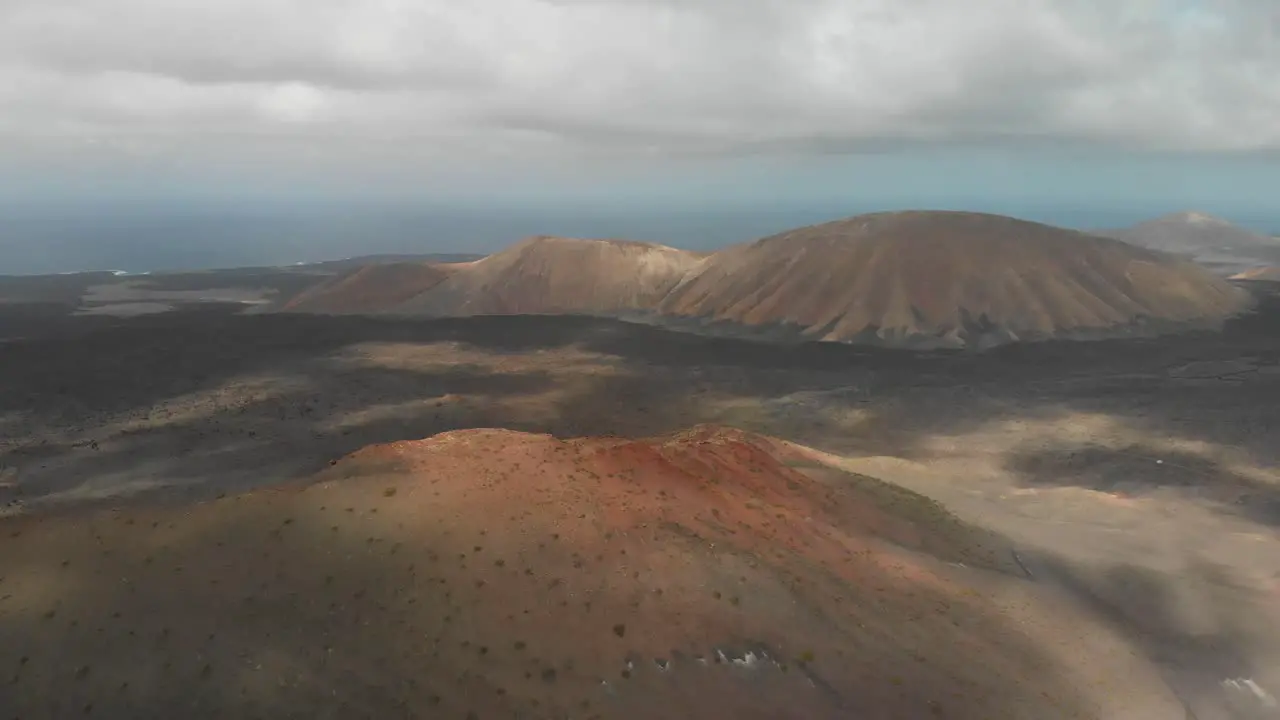 Pull back drone shot descending behind a red volcano on a cloudy day