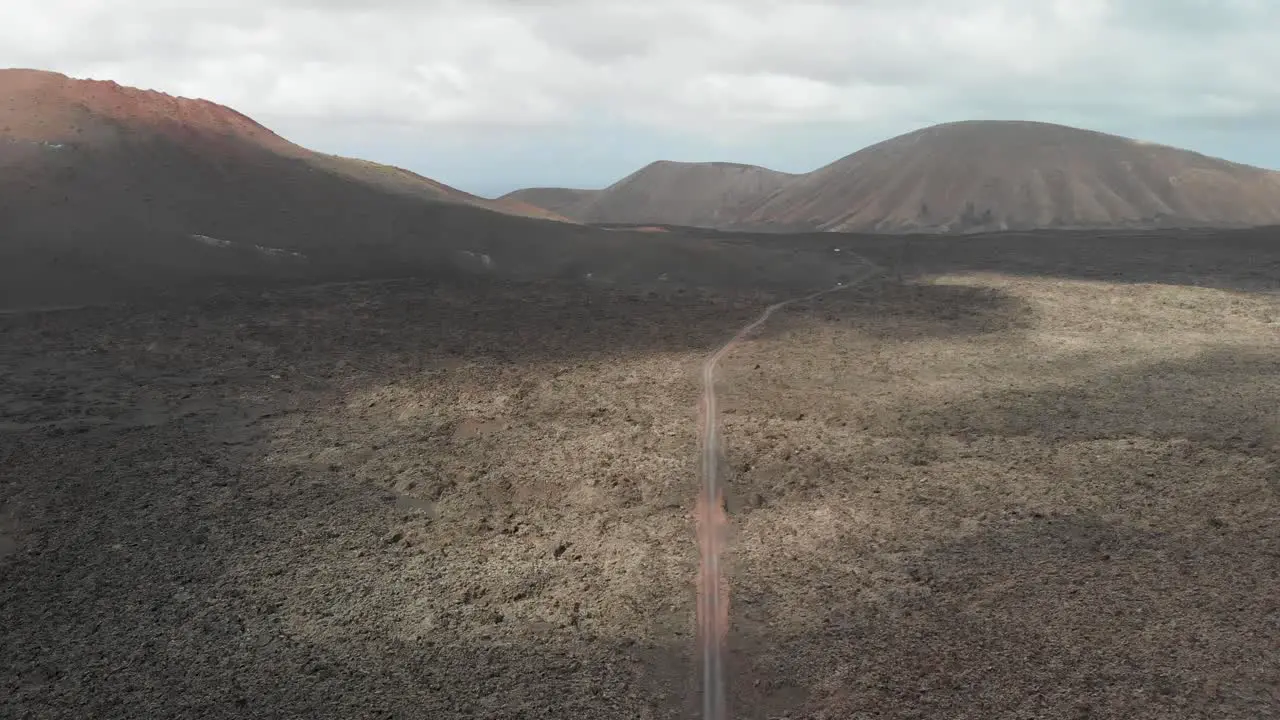 Ascending and turning aerial shot of a barren volcanic field with a dirt road