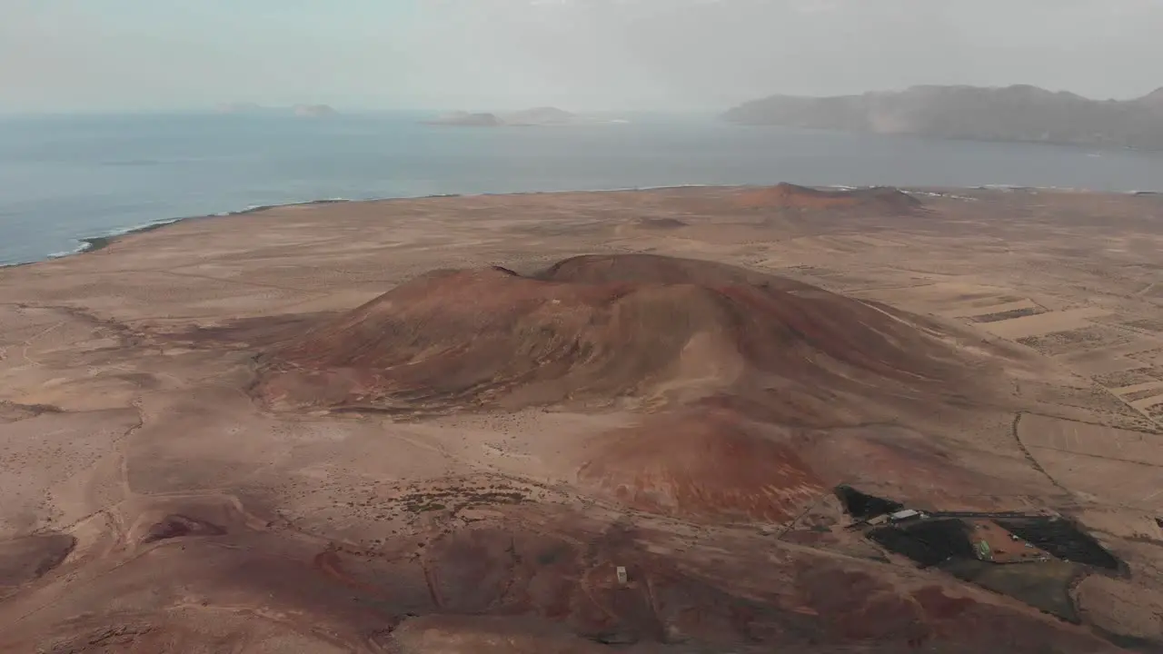 Pull back and descending drone shot behind a red volcano with small white building on top