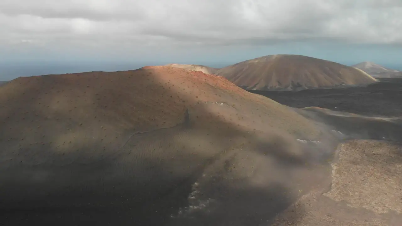 Ascending drone shot over a red volcano revealing the ocean