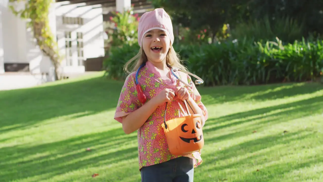 Video of happy caucasian girl in nurse costume holding halloween trick or treat basket in garden