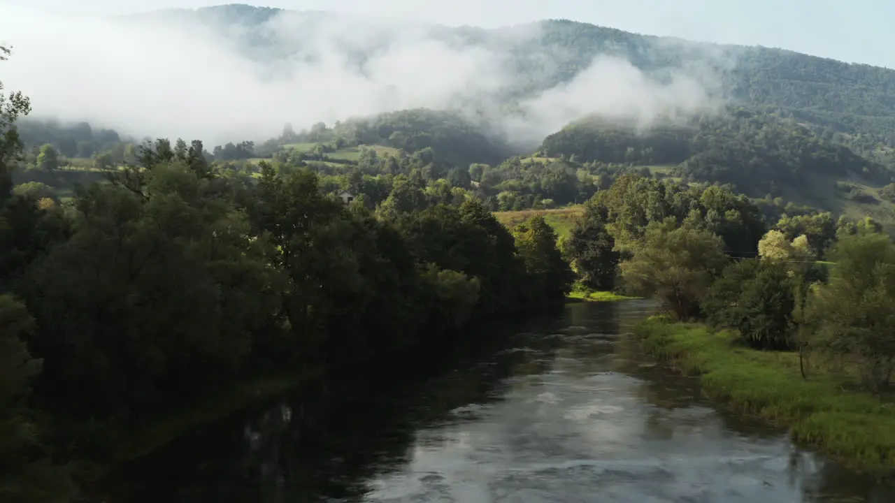 Magical flight at sunrise over water stream in lush hills with low fog