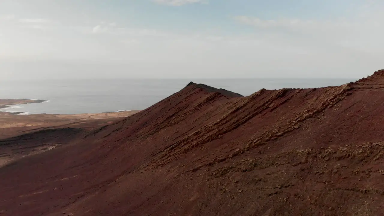 Pull back drone shot of a red volcano by the ocean