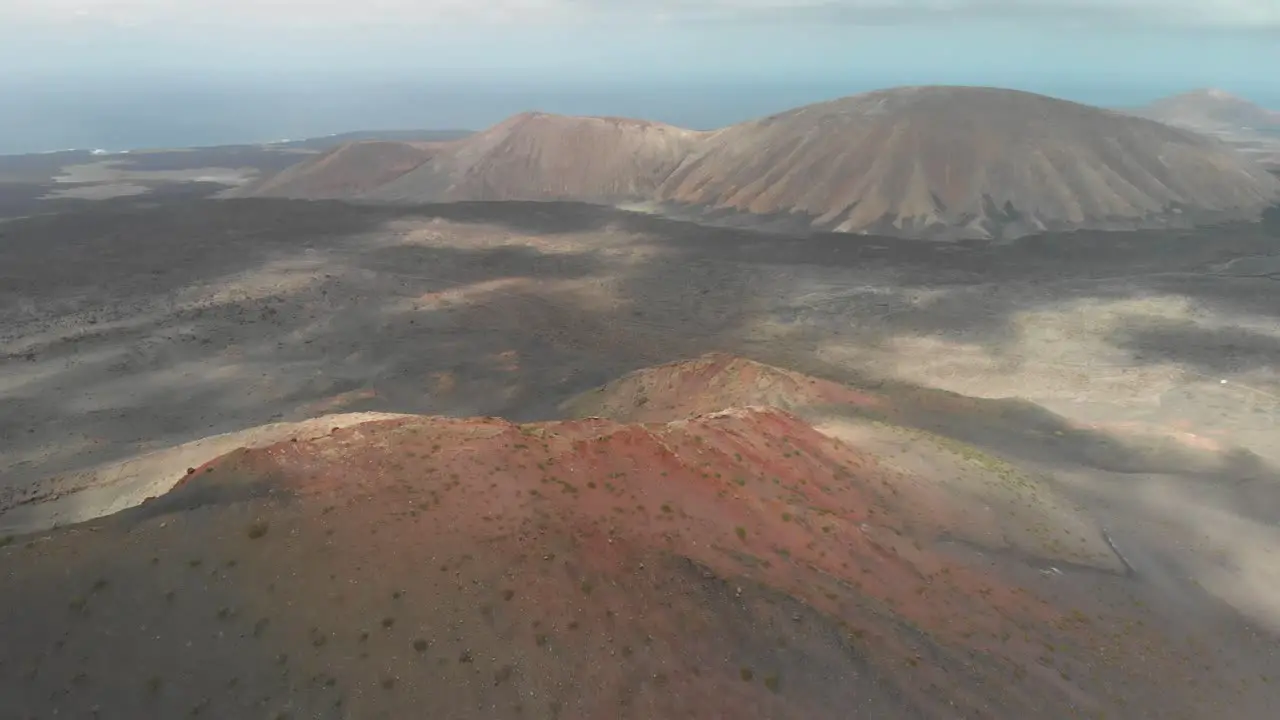 Panning up drone shot of a red volcano by the ocean on a cloudy day