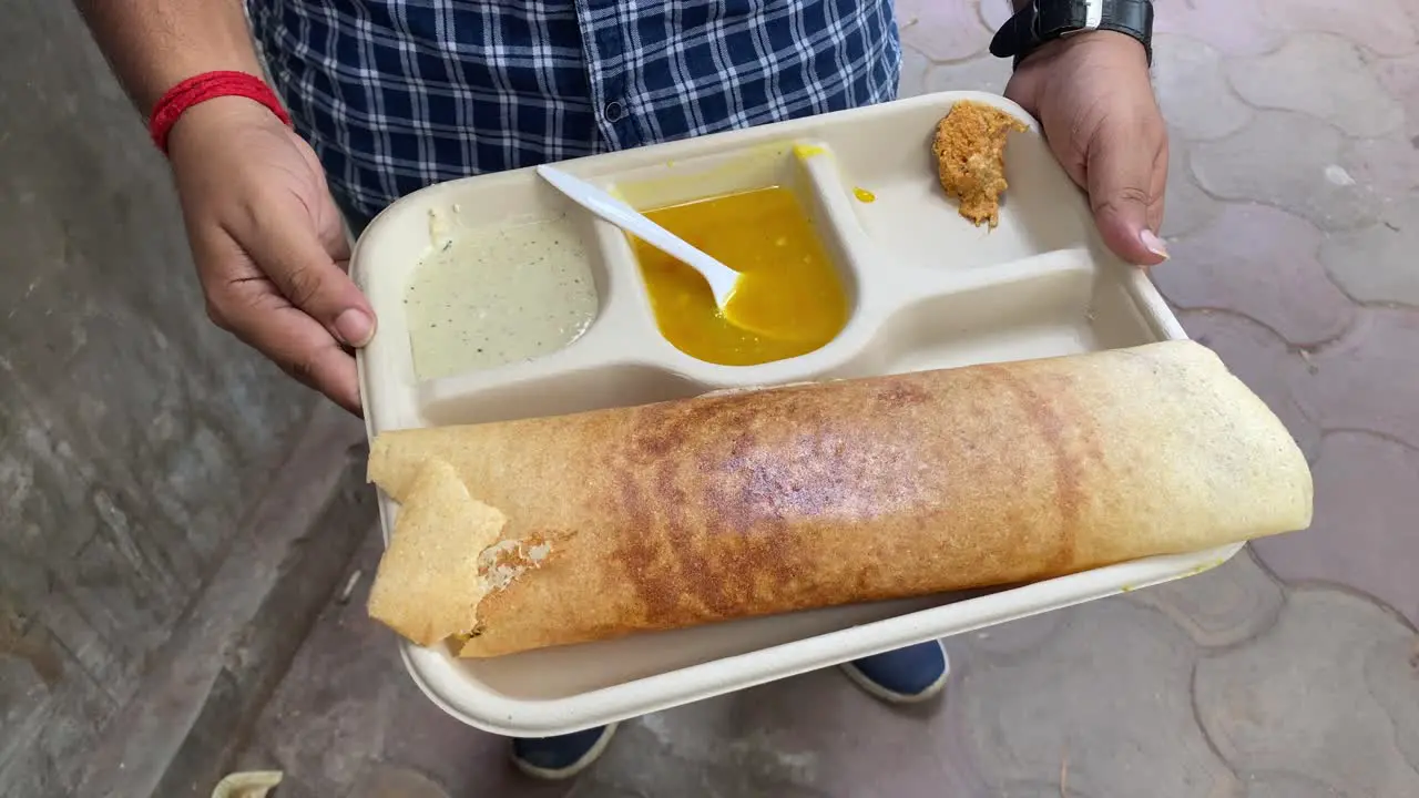 Masala Dosa a popular South Indian dish prepared of rice lentils potatoes Methi and curry leaves and served with chutneys and sambar is being held in a man's hand