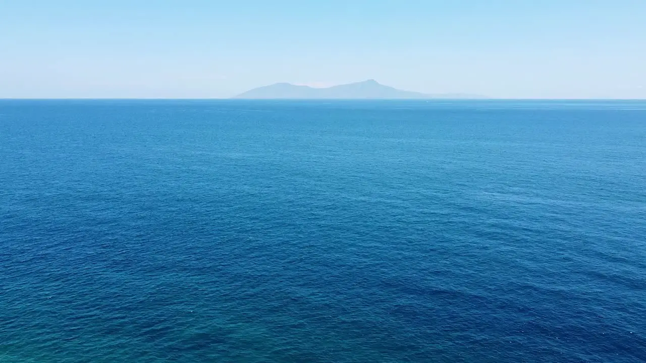 Aerial drone rising over vast blue ocean and rugged remote tropical Atauro Island in the distance as seen from capital Dili Timor Leste Southeast Asia