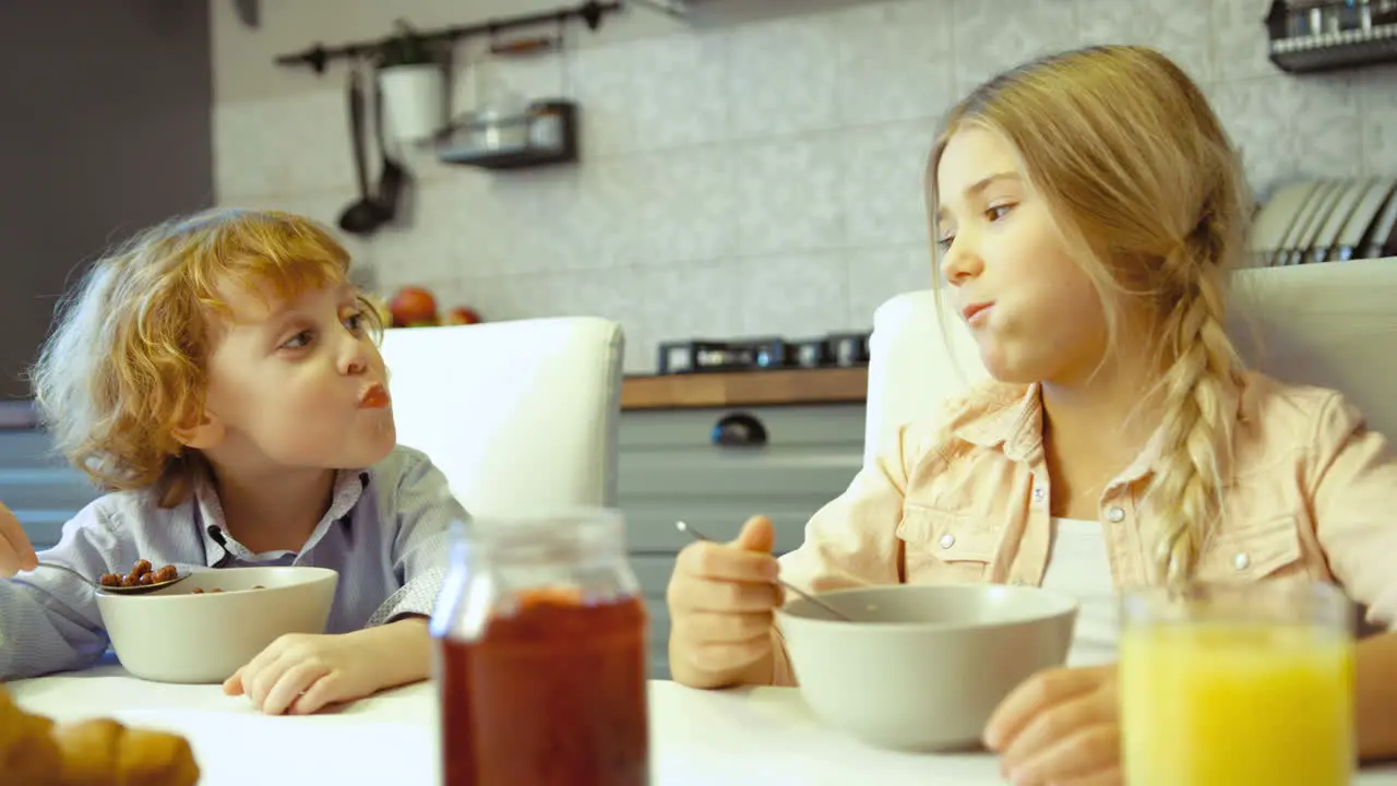 Two Siblings Having Cereal With Milk For Breakfast In The Kitchen