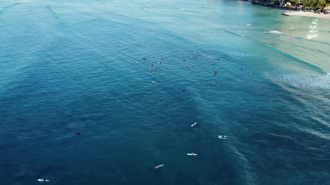 4K cinematic drone reveal shot panning from surfers trying to catch a wave at Waikiki Beach to the Oahu coastline