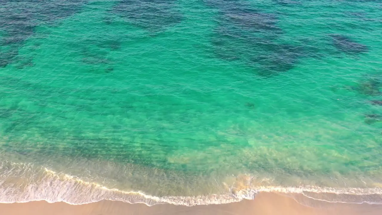 Aerial view of tropical white sandy beach with soft waves hitting the shore