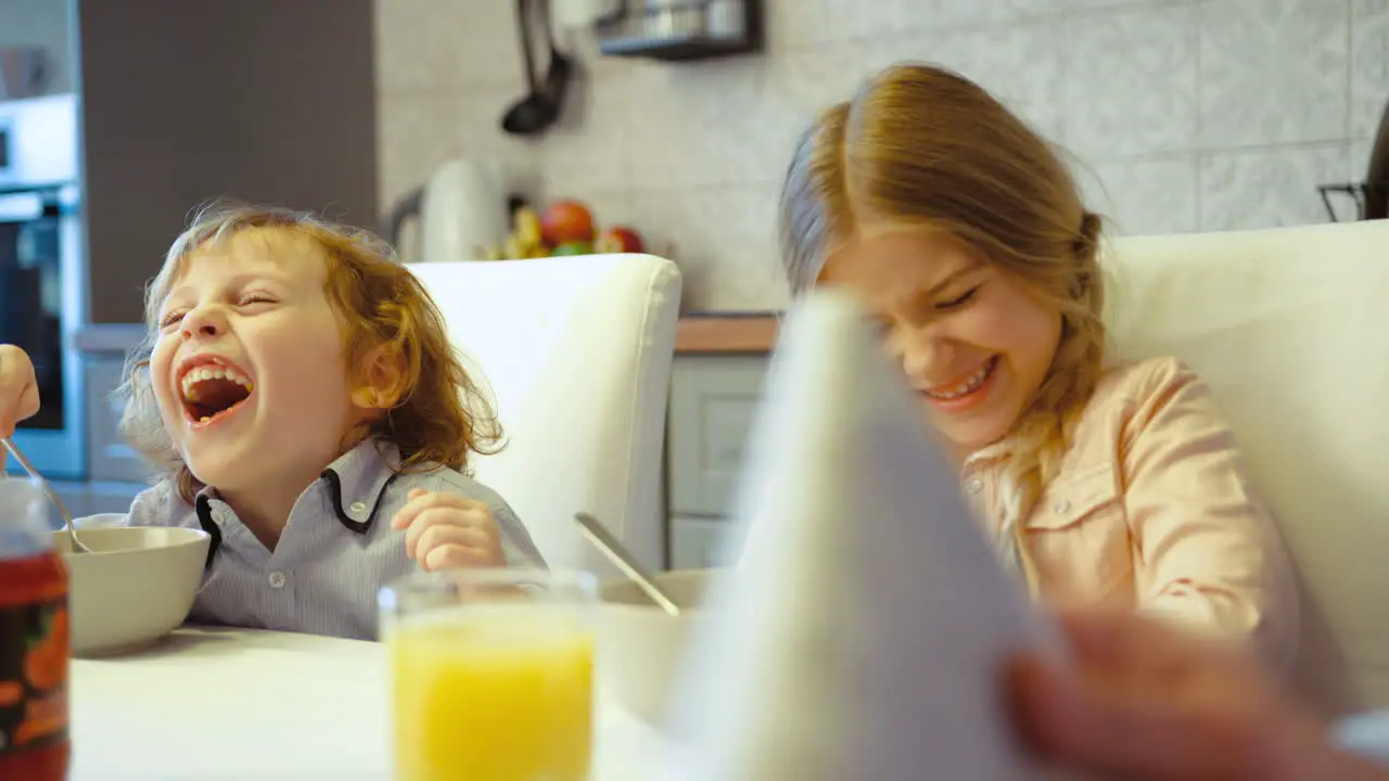 Two Siblings A Boy And A Girl Having Breakfast And Laughing In The Kitchen