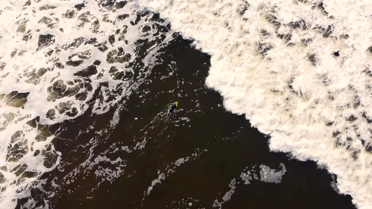 Bird's-eye drone shot of surfer duck diving with surfboard under brown foam storm water ocean waves in Birdie Beach Munmorah State Conservation Area Central Coast NSW Australia 3840x2160 4K