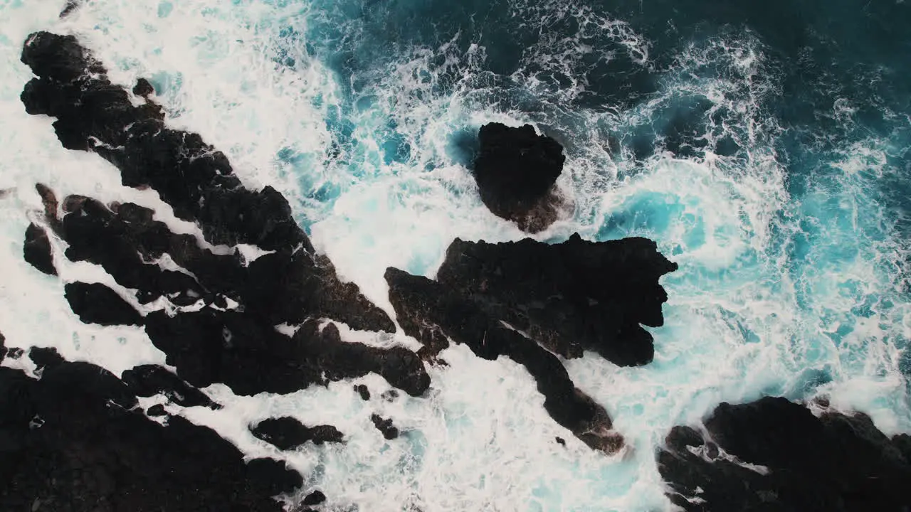 Top down aerial shot of white water crashing around dark lava rocks in Hawaii