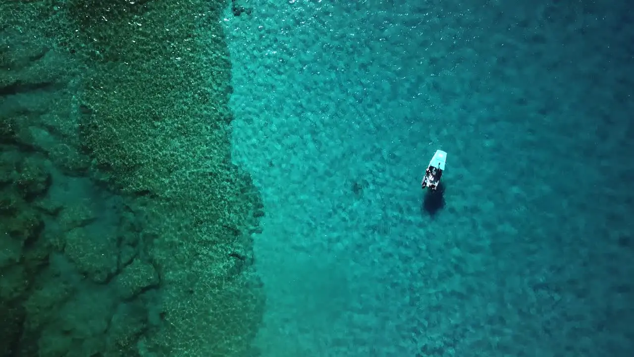 Rising aerial view of a boat floating above a coral reef above crystal clear water