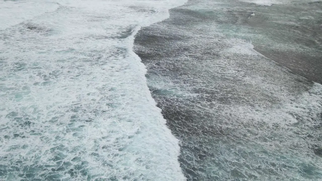 Aerial flight following waves rolling onto the beach with whitewash