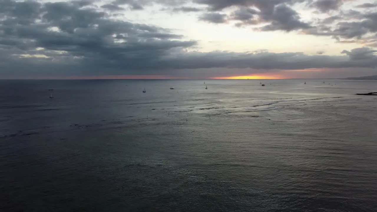 4K cinematic drone shot of the sun setting over the ocean as sailboats sit enjoying the view near Waikiki beach in Oahu