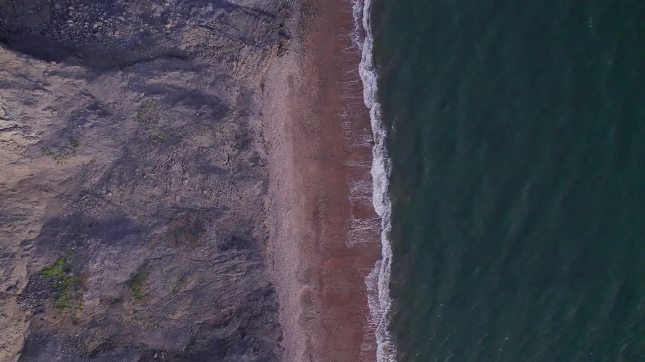 Top down drone shot moving down of green sea's waves and cliffs on the Jurassic Coast Dorset UK