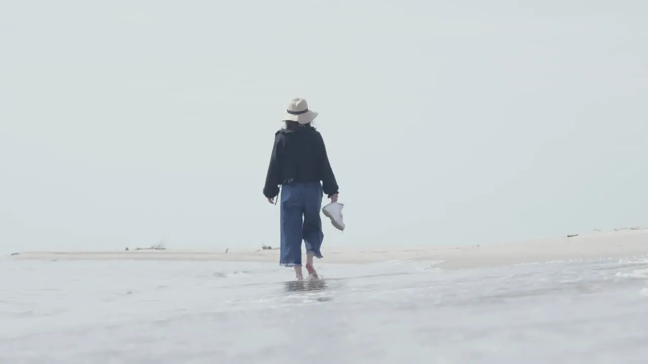 a women walk alone barefoot on the beach with the waves