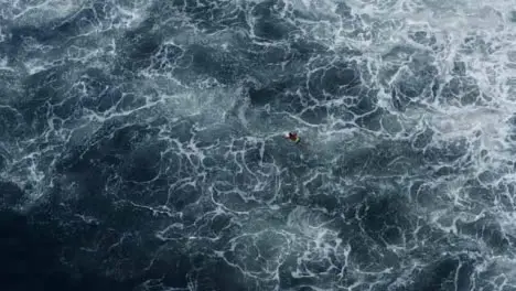 Drone Shot Looking Down On Surfer Swimming Against Waves