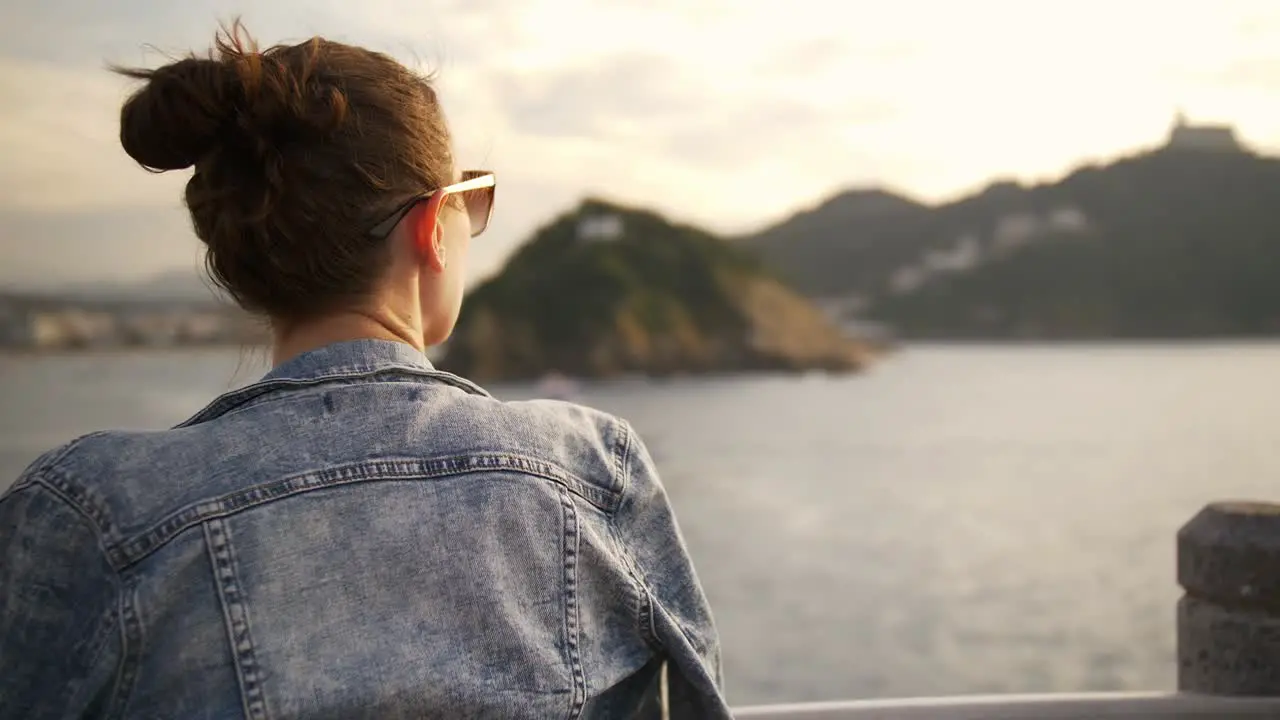 Girl looking out over harbour coastline during sunset in San Sebastian Spain Europe boats on the water in a light breeze in the warm sun handheld shot