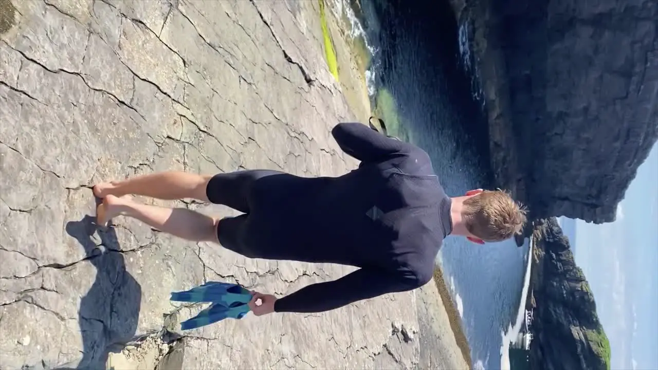 Man in wetsuit carrying snorkeling gear walks to coastline