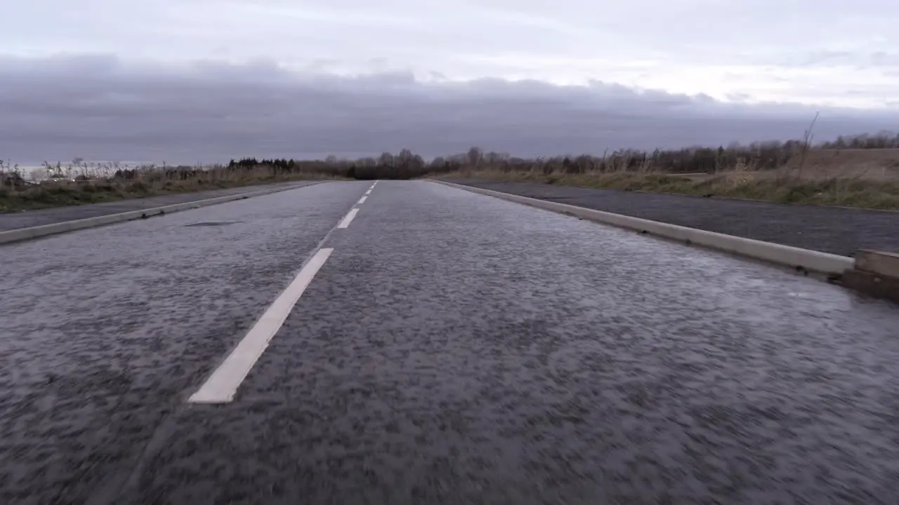 Low angle flying above empty road markings asphalt pavement long into distant horizon