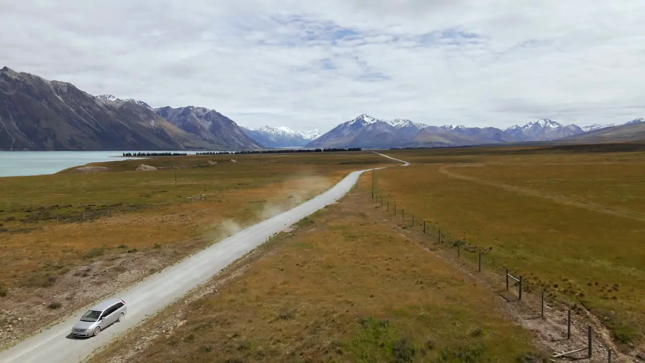 Silver van on dusty picturesque dirt road with snow-capped mountains in background