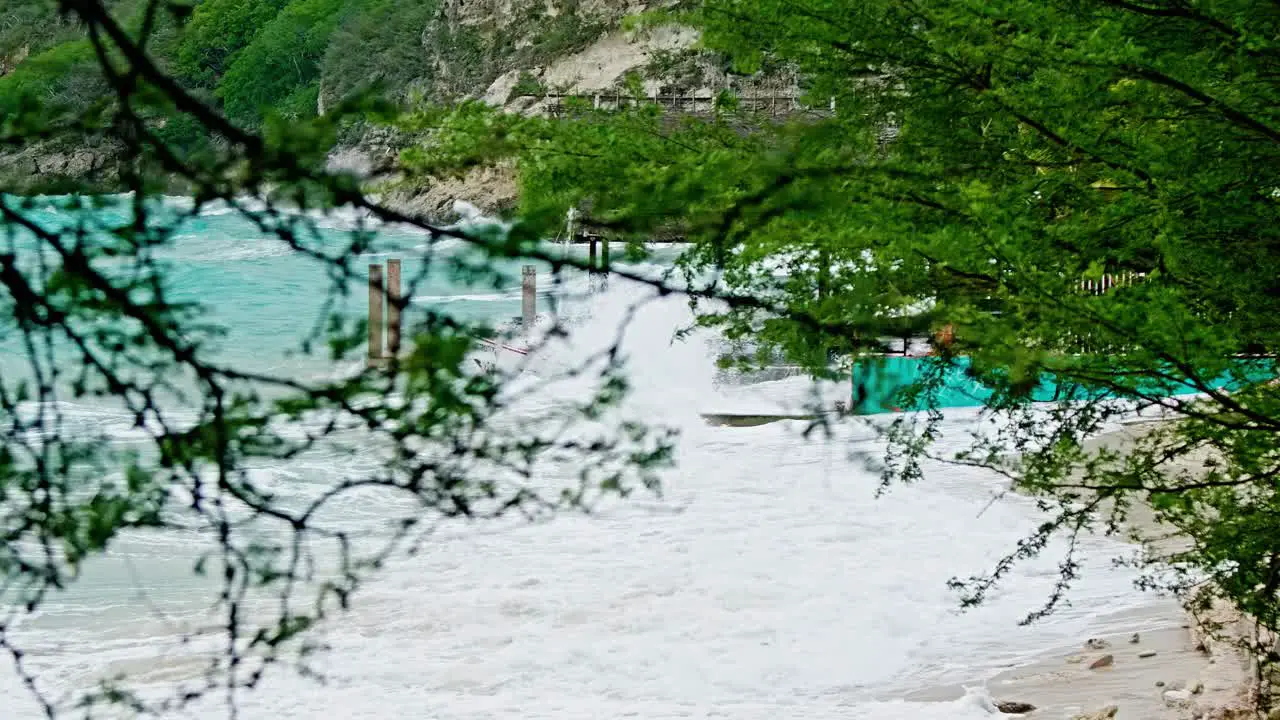 Zoom shot with foliage foreground of local wooden fishing boat being smashed into land during sudden storm with rough waves Caribbean