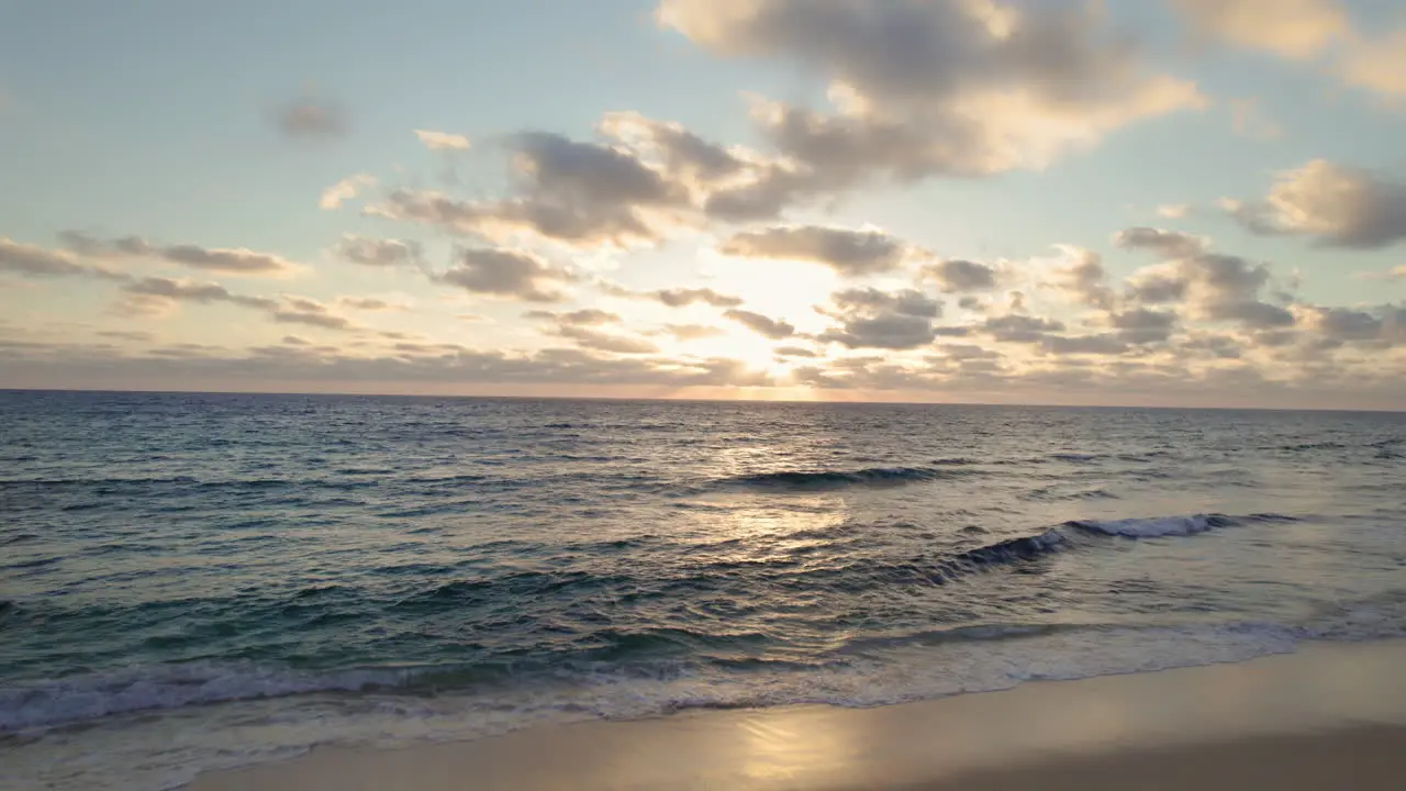 Aerial shot of an ocean at sunrise revealing a sandy beach and a lifeguard house with clouds in the sky