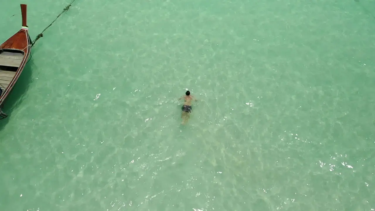 Man swiming breaststroke near a boat on clear ocean water in slow motion