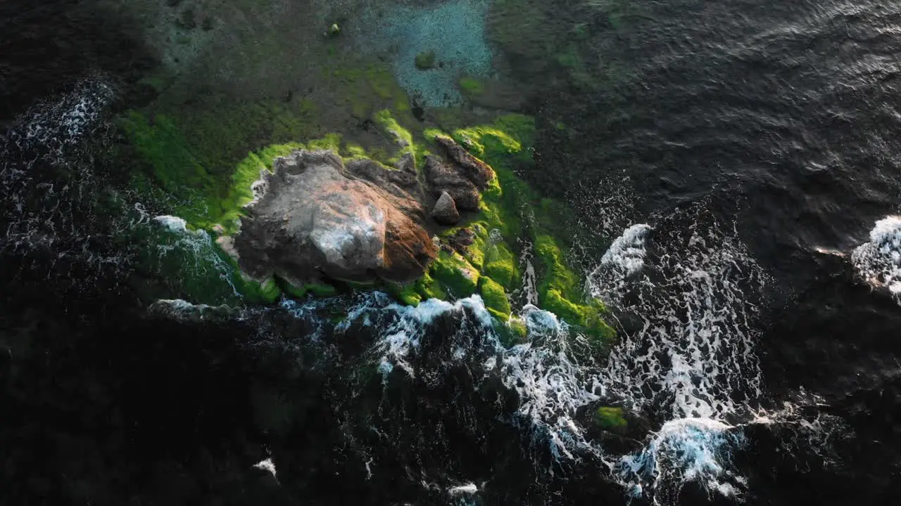 Arc aerial shot over rock in the sea at sunset bright colors and dark water