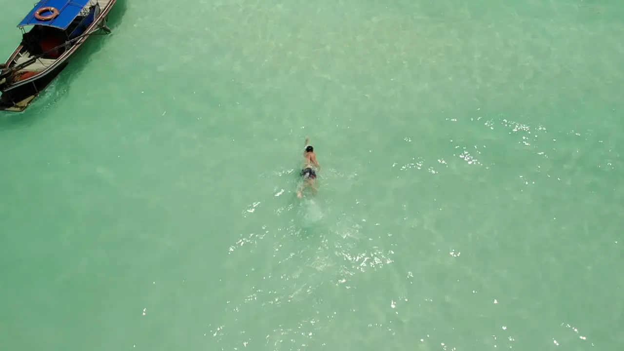 Man freestyle swim in clean ocan waters near a boat in Thailand