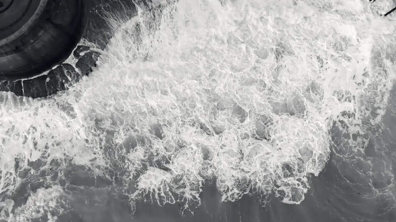 Aerial footage of waves crashing against a sea wall in monochrome