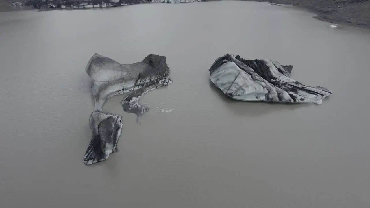 Aerial view over blackned ice blocks on the Solheimajokull glacier lagoon tilt drone shot