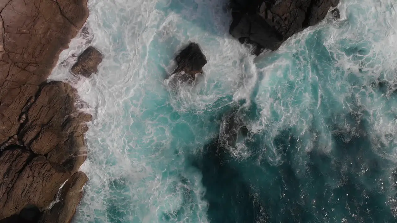 Top down aerial rising shot over strong ocean waves breaking against cliffs