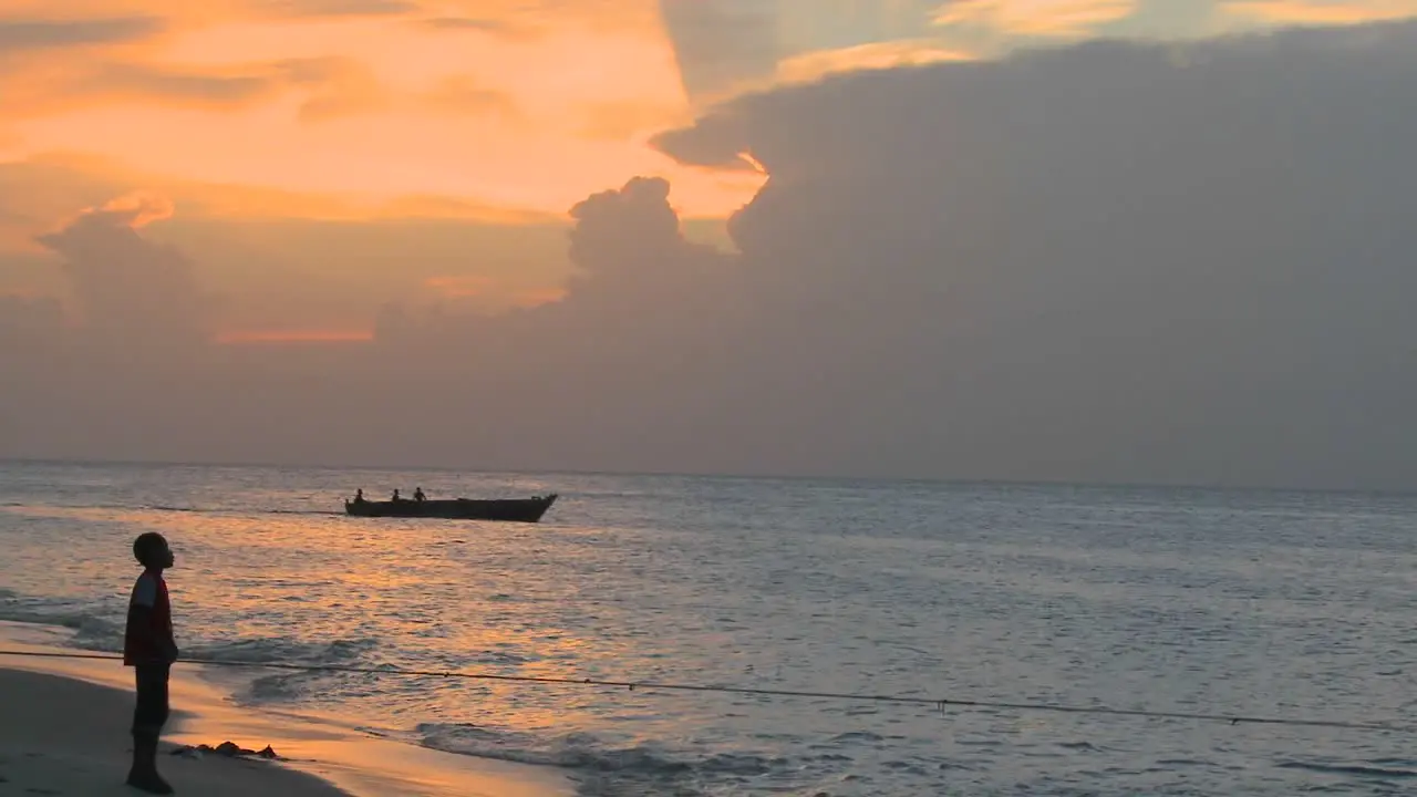 A small motorboat heads out at sunset as people walk on the beach at Stone Town Zanzibar