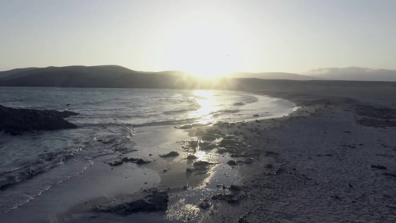 Beautiful shot of the shoreline of a beach during sunset as the waves crash against the rocks and the sun lights up the sea