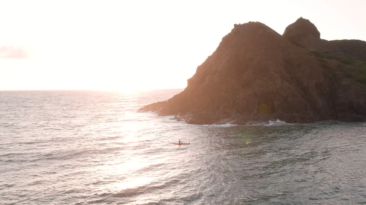 Man kayaking along Moku Nui islet in Hawaii at sunrise zooming aerial