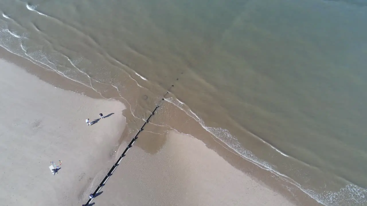 Tourists walking on sunny aerial view looking down over golden sandy beach tide