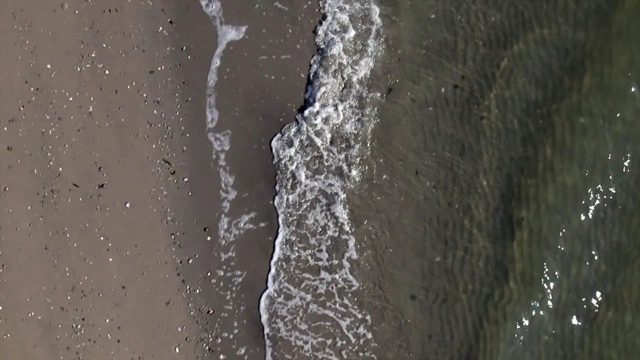 A top down view over an empty beach as the waves gently crash onto the shore in slow motion