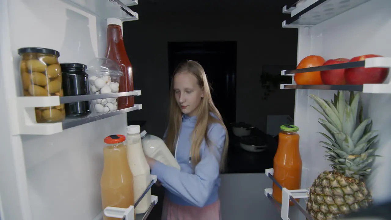 The child takes a bottle of milk from the refrigerator View from inside the refrigerator