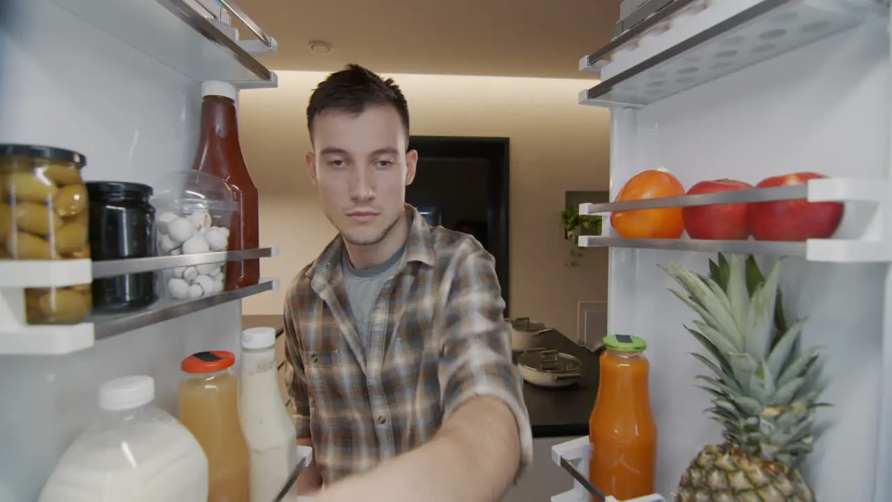 A young man takes a container with breakfast from the refrigerator View from inside the refrigerator