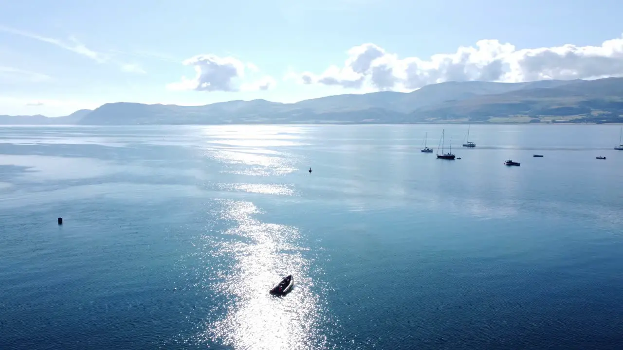 Snowdonia clear mountain range aerial panning right view across sunny calm Welsh shimmering seascape