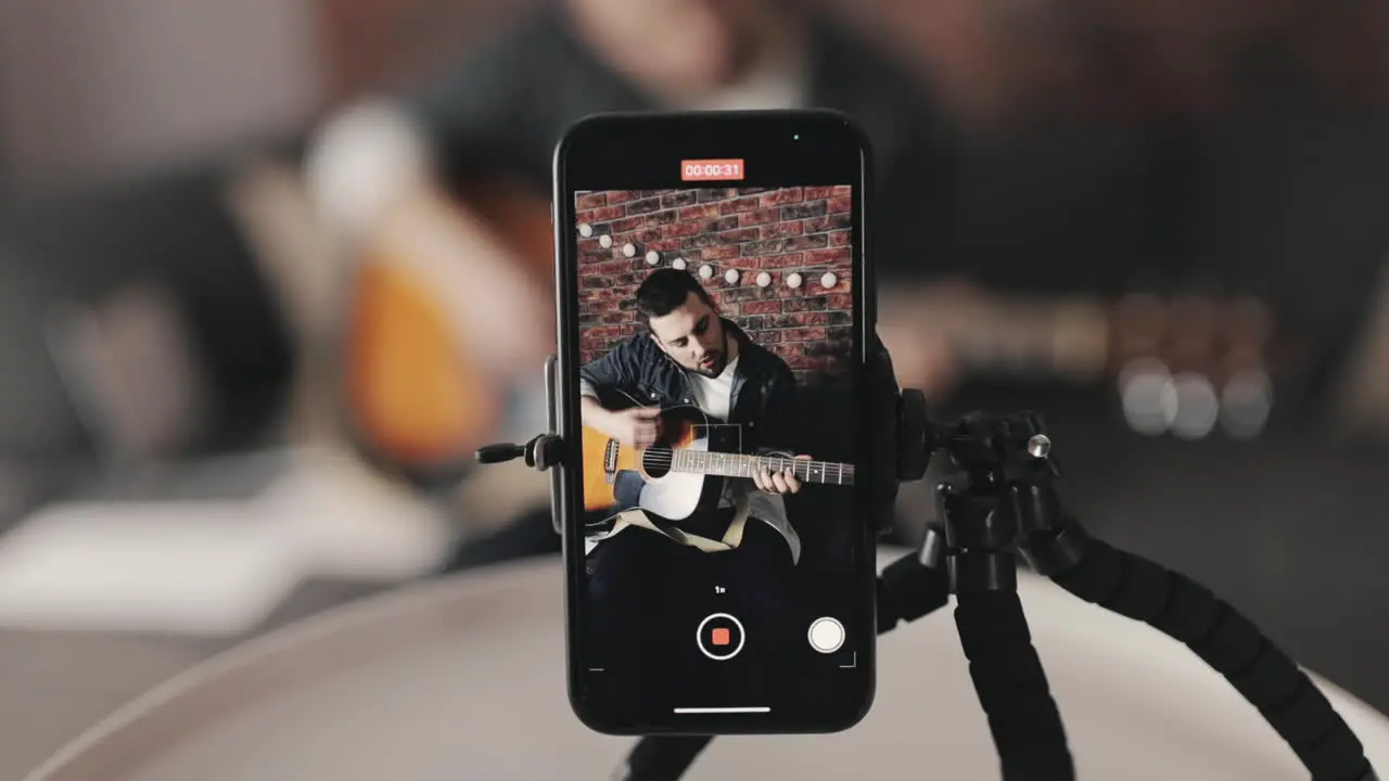 Joven Músico Masculino Transmitiendo Un Video Tutorial Tocando La Guitarra En Casa