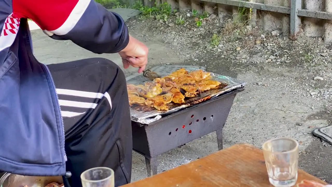 A peasant in a dirty clothes grills chicken rural Croatia