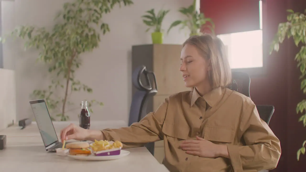 Working Pregnant Woman Eating Potato Chips While Sitting At Desk In The Office