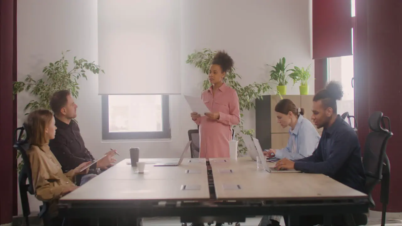 Pregnant Woman Explaining A Project In Front Of Her Coworkers In A Meeting Room 3